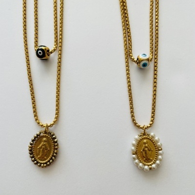Dois colares dourados com pendentes ovais e contas de olho turco sobre fundo branco.