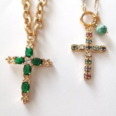 Dois colares com cruzes, um com pedras verdes e outro com pedras multicoloridas em corrente dourada.