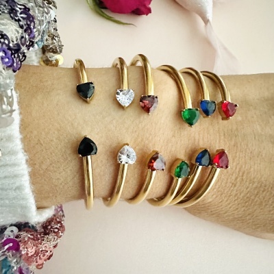 Braceletes dourados com pedras em forma de coração coloridas no pulso