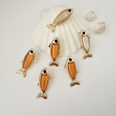 Broches em forma de peixe com corpo laranja e branco sobre conchas brancas