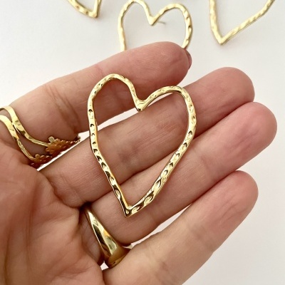 Corrente ou anel em forma de coração dourado com textura martelada numa mão sobre fundo branco