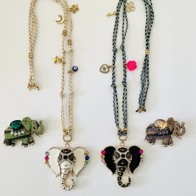 Dois colares com pingentes de elefantes e dois broches de elefantes coloridos sobre fundo branco.