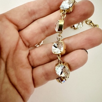 Pulseira dourada com cristais transparentes grandes em diferentes cortes segurada por uma mão