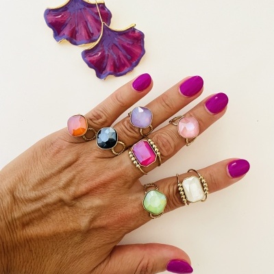 Mão com anéis coloridos e brincos roxos em forma de folha