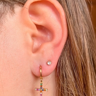 Orelha com brinco pequeno de bola e brinco de cruz dourado com pedras coloridas