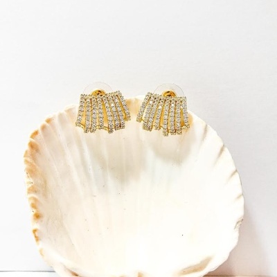 Brincos dourados com pedras pequenas dentro de uma concha branca