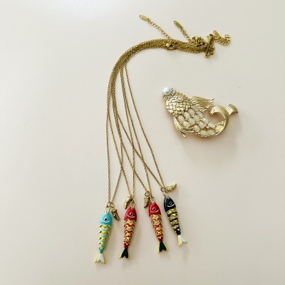 Cinco peças de joalharia em forma de peixe, quatro colares coloridos e um broche dourado com pedras e pérola