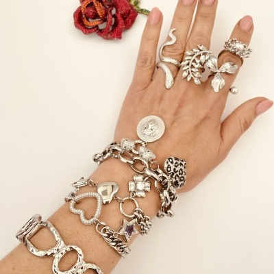 Mão feminina com anéis e pulseiras prateadas variadas e flor vermelha em tecido no fundo branco