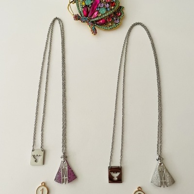 Dois colares com pingentes triangulares e um broche colorido em fundo branco