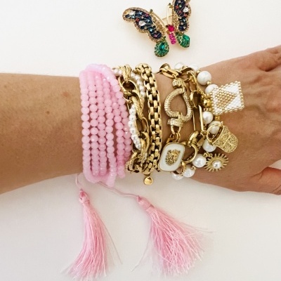 Pulseiras douradas e rosas com diferentes texturas e pingentes, e um broche de borboleta colorida.