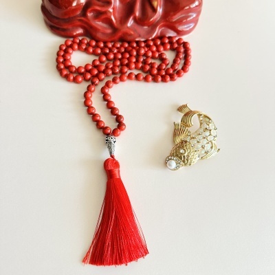 Colar de contas vermelhas com tassel e broche dourado em forma de peixe.