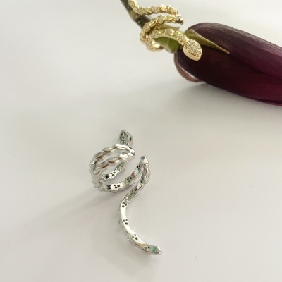 Anéis em forma de serpente dourado e prateado com textura facetada sobre fundo branco com flor roxa