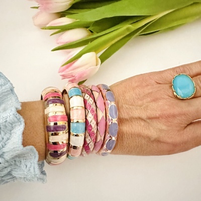 Pulseiras e anel coloridos em mão com flores ao fundo