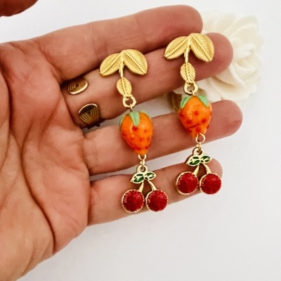 Brincos dourados com morangos e cerejas segurados numa mão