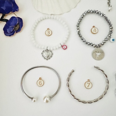 Pulseiras variadas em branco, prata e brilho metálico com pendentes e olhos turcos numa superfície branca.