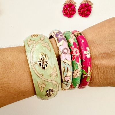 Pulseiras esmaltadas coloridas com padrão floral e brincos vermelhos ao fundo