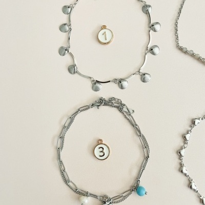 Colares e pulseiras em metal prateado com pendentes variados sobre fundo claro.