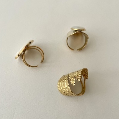 Três anéis dourados, dois com pedra branca no topo e um com padrão texturizado de folhas
