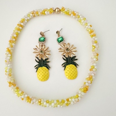Conjunto de bijuteria com colar de contas amarelas brancas laranja e brincos com abacaxi e flores douradas