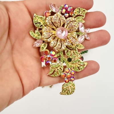 Broche dourado com pedras rosa, verdes e vermelhas em forma de flor na mão