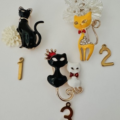 Pins de gatos em esmalte preto, amarelo e branco com detalhes dourados e pedras, com números metálicos 1, 2 e 3