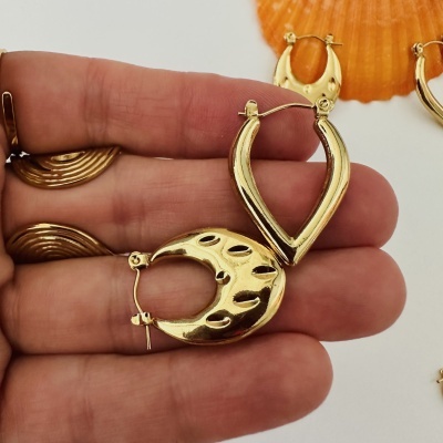Brincos de argola dourados em mão com concha laranja ao fundo