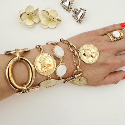 Pulseiras e anel dourados com detalhes e brincos em forma de coração prateados e flores creme
