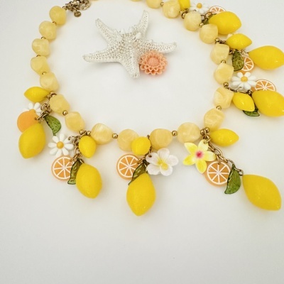 Colar amarelo com penduricalhos de limão, flores e folhas em fundo branco com estrela-do-mar.