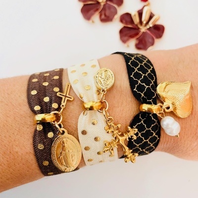 Pulseiras de tecido com pendentes dourados em pulso.