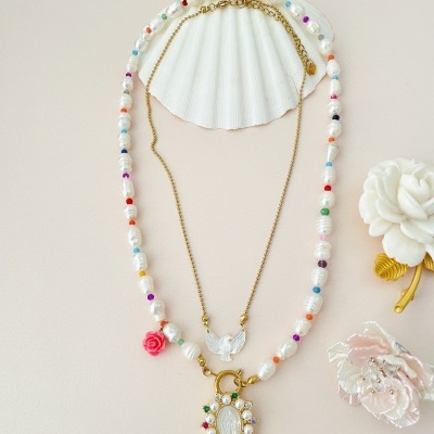 colar de pérolas coloridas e dourado com pendentes sobre fundo bege com concha e flores