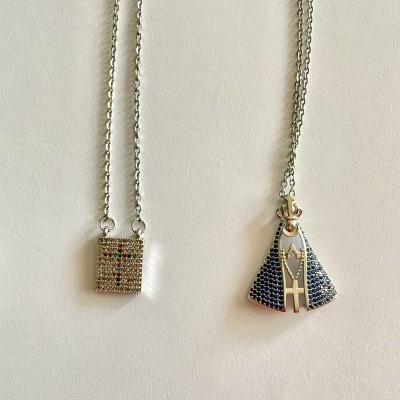 Dois colares prateados com pendentes distintos sobre fundo branco