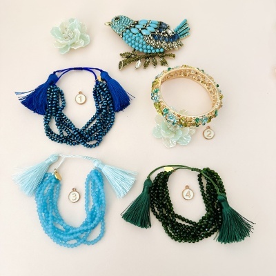 Quatro pulseiras coloridas com franjas, anel flor verde claro e broche de pássaro azul sobre fundo claro