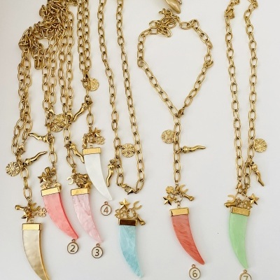 Sete colares dourados com pendentes coloridos em forma de dente numerados de 1 a 7.