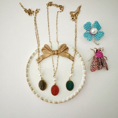 Três colares dourados com pendentes coloridos e dois broches decorativos em fundo branco