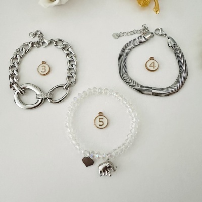 Três pulseiras prateadas e transparente com diferentes designs e etiquetas numeradas em fundo branco