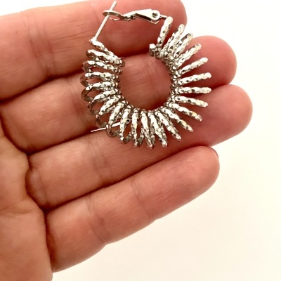 Brinco prateado texturizado em forma de espinhos sendo segurado na mão