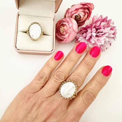 Anel dourado com medalha religiosa branca e caixa de veludo rosa ao lado com flores rosas