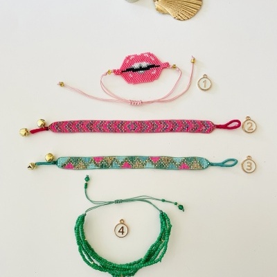 Quatro pulseiras coloridas com contas e fechos de cordão sobre fundo branco com concha e frasco