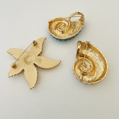 Broches dourados em forma de concha e estrela-do-mar sobre fundo branco