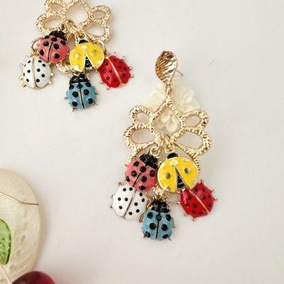 Brincos dourados com joaninhas coloridas penduradas.