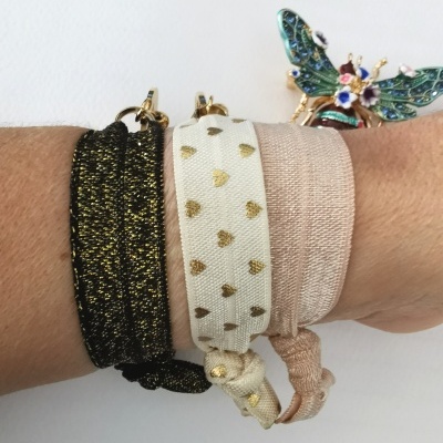 Três pulseiras elásticas com cores e padrões distintos num pulso, com broche de inseto colorido ao fundo