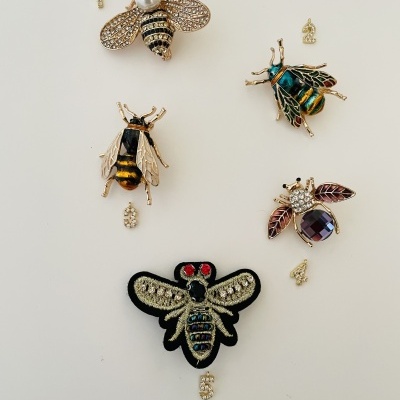 Cinco broches de abelhas e números dourados em fundo branco