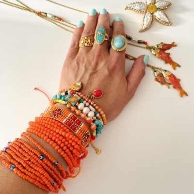 Mão com anéis e pulseiras coloridas e colares dourados com pendentes sobre fundo branco