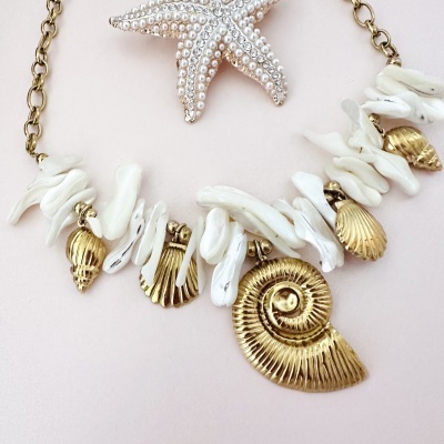 Colar com conchas douradas e branquinhas sobre fundo claro com estrela do mar decorativa