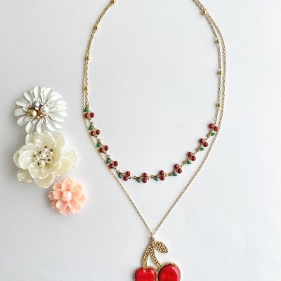 Colar duplo dourado com pendente de cerejas vermelhas e pequeno padrão decorativo, flores decorativas ao lado