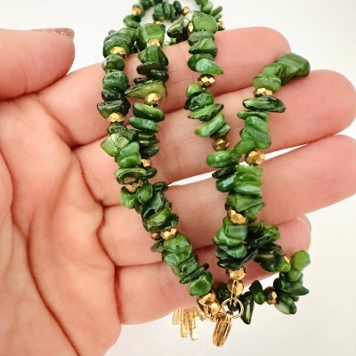 Pulseira de pedras verdes e contas douradas na mão