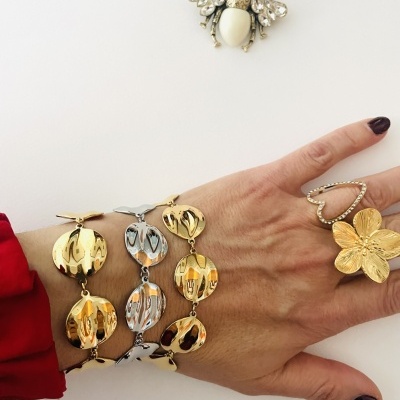 Pulseiras douradas e prateadas, anéis dourados e broche de abelha sobre mão feminina