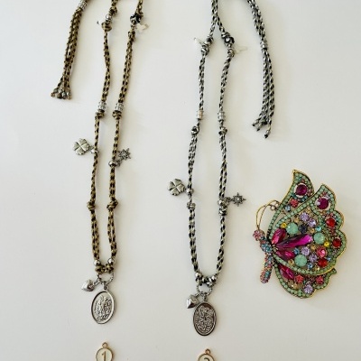 Dois colares com medalhões e um broche de borboleta colorido sobre fundo branco