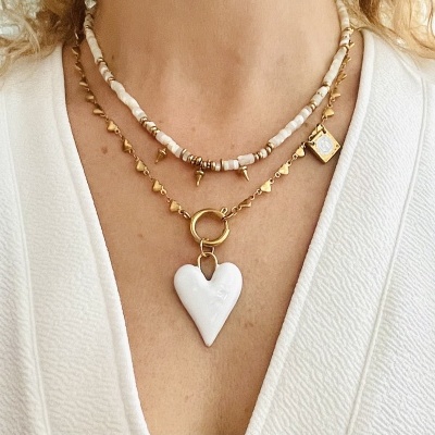 Colares dourado e de contas com pendentes no pescoço de pessoa com roupa branca