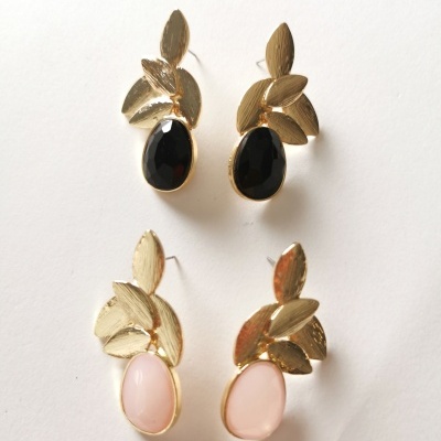 Brincos dourados com pedras preta e rosa e design de folhas sobre fundo branco